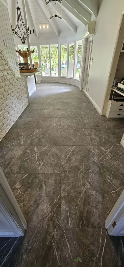 Dark marble-look porcelain floor tiles running through a hallway into a curved sunroom with white brick wall and vaulted ceiling by Dakom Tiling Auckland